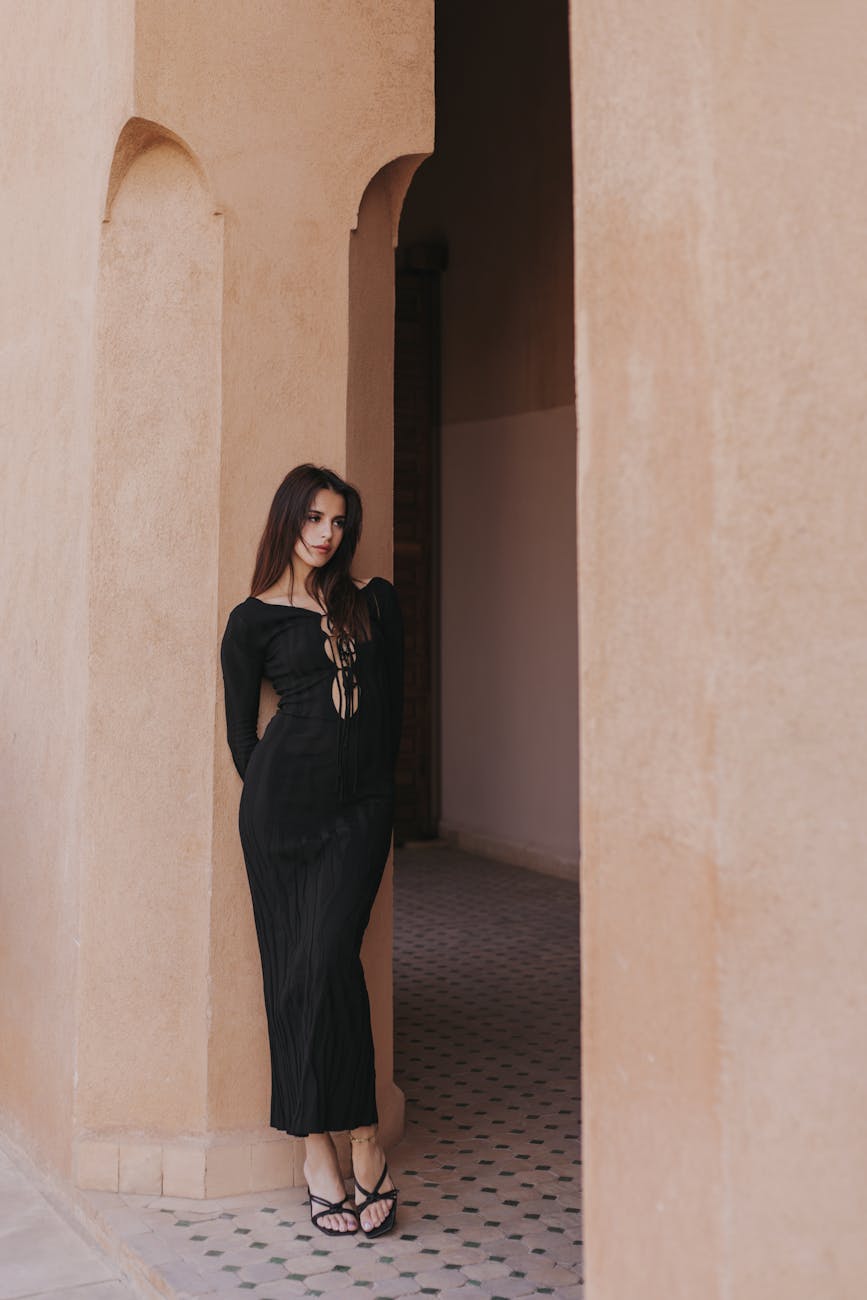 woman wearing a black dress leaning against a beige wall in marrakesh